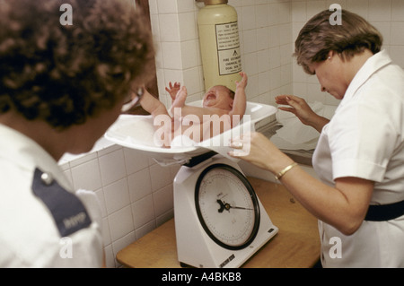 A nurse weighs a crying baby boy whilst a prison officer looks on. Stock Photo