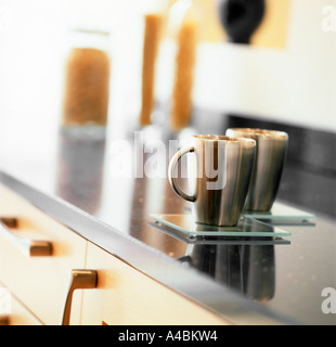 A modern kitchen scene featuring two stainless steel coffee mugs on a modern kitchen work surface pasta jars in the background Stock Photo