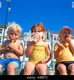 Children kids eating ice cream icecream cones on a hot summers day sitting on the sea wall at Aberystwyth Wales UK KATHY DEWITT Stock Photo