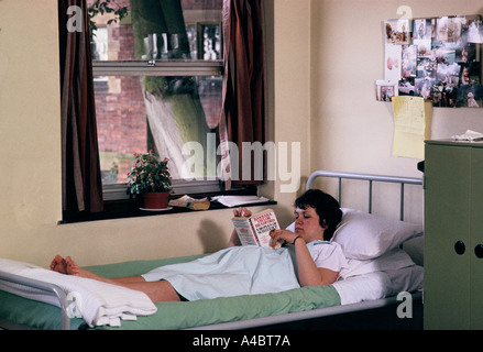 A pregnant inmate lies in bed reading A Woman Of Substance by Barbara Taylor Bradford. Stock Photo