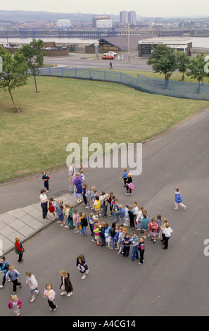CHILDREN IN A PRIMARY SCHOOL PLAYGROUND LINE UP BEFORE THE BEGINNING OF CLASS. Stock Photo