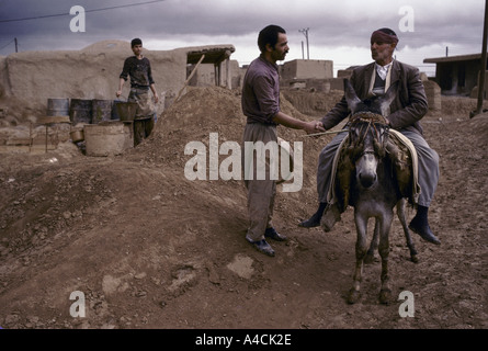A potter talks to a passing friend riding on a donkey while the potter's assistant cleans equipment in the background, Lalejin Stock Photo