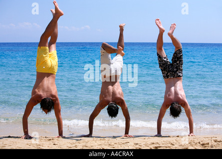 Three young men doing handstands on beach Stock Photo