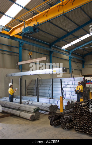 Two industrial workers, moving metal parts with remotely controlled crane in industrial warehouse. Daylight. Stock Photo