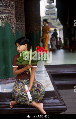 A young woman sitting holding flowers at Shwedagon Paya Temple, Yangon, Rangoon, Myanmar, Burma Stock Photo