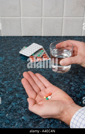A man's hands holding pills and a glass of water Stock Photo