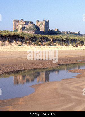 Historical coastal Bamburgh Castle landscape reflection in sandy beach low tide water pool & sand dunes on scenic Northumberland coastline England UK Stock Photo