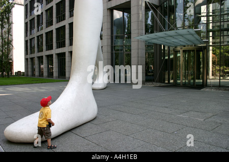 kid impressed by big foot Walking Man in front of Muenchener Rueckversicherung Munich Re Bavaria Germany Stock Photo