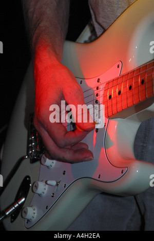 Guitarist playing an electric guitar on stage under a red spot light Stock Photo