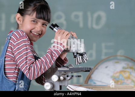 Caucasian female student sitting at desk in class with microscope Stock Photo