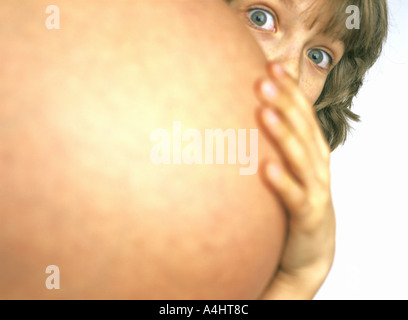 Young boy plays hide and seek behind pregnant mother Stock Photo