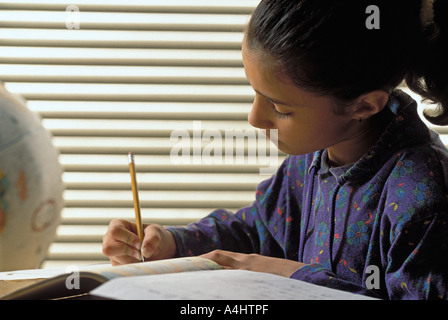 Portrait Latino female student writing at desk in middle school classroom Stock Photo