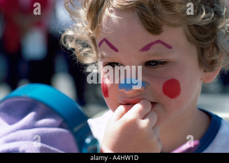 Unsure Young Child looking pensively in a Mirror at Face Painting Stock Photo