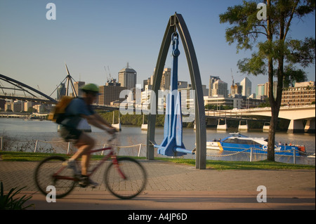 Cyclist riding along the River Walk as a CityCat catamaran passes on the Brisbane River. Stock Photo