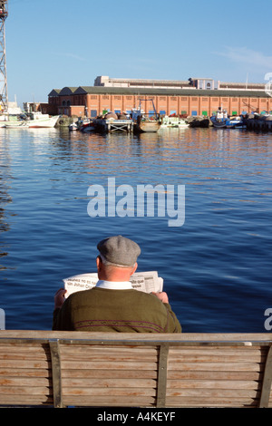 Spain, Barcelona, man sitting on bench reading newspaper by the water Stock Photo
