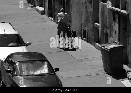 Old man walking with bike on sidewalk, rear view Stock Photo