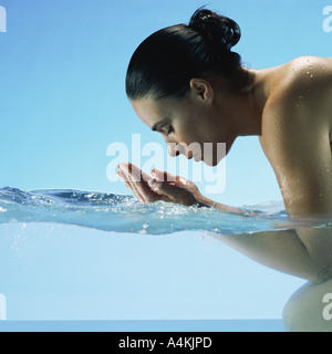 Woman kneeling in water, cupping hands to face Stock Photo