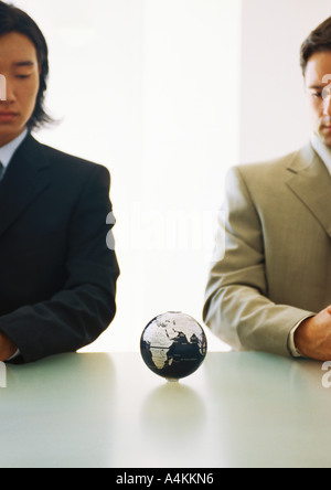 Two businessmen looking down at small globe on table Stock Photo