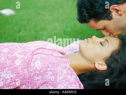 Woman lying on grass, man kissing her forehead Stock Photo