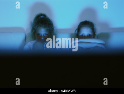 Children sitting on sofa, hugging knees, watching television partial view Stock Photo