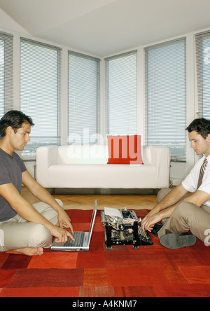 Man using laptop computer and second man using typewriter, side view Stock Photo