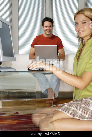 Woman kneeling on floor, holding computer mouse, side view, man using laptop computer in background Stock Photo