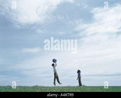 Young man and woman on grass in distance playing with ball, man jumping to catch ball Stock Photo