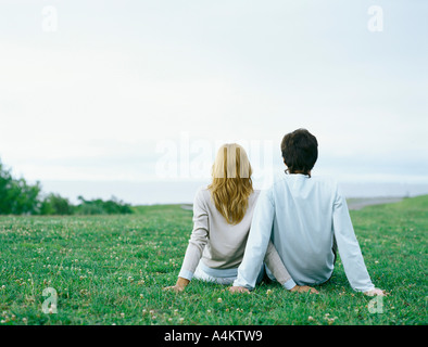 Young man and young woman sitting side by side on grass, propped up with hands, rear view Stock Photo