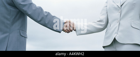 Woman and man in suits shaking hands, mid-section with sky in background Stock Photo