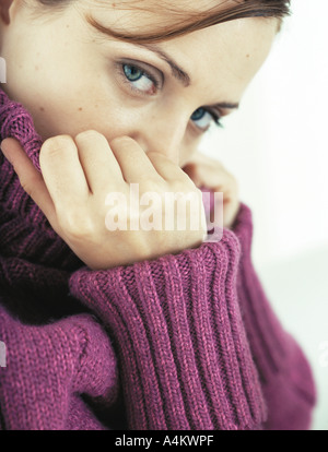 Woman covering part of face with neck of sweater, looking at camera, close-up Stock Photo