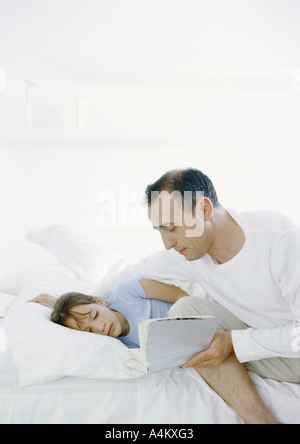 Man sitting on edge of bed reading book to girl lying in bed Stock Photo