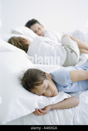 Girl and boys lying down on bed Stock Photo