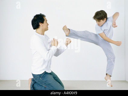 Boy giving karate kick in mid air, man on knees with fists out Stock Photo