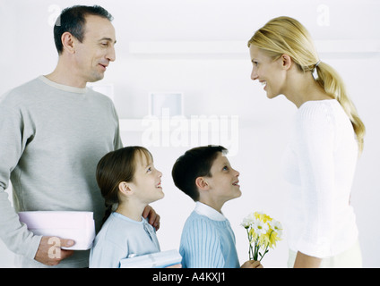Man with boy and girl facing woman with gifts and flowers Stock Photo