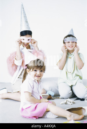 Mother sitting on floor with boy and girl, wearing party hats and disguises Stock Photo