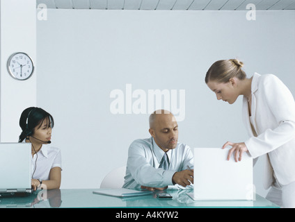 Colleagues looking at document together, woman working on laptop nearby Stock Photo