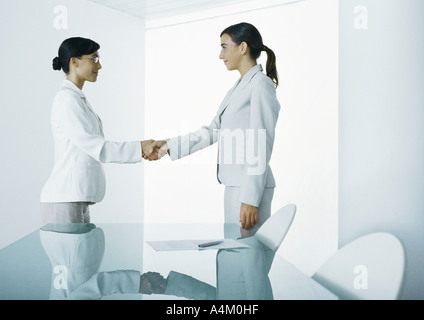 Two young women in suits shaking hands Stock Photo