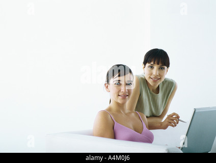 Woman sitting on sofa with laptop, second woman behind leaning on sofa Stock Photo