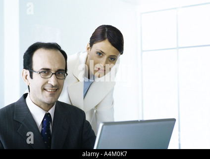 Businessman and businesswoman with laptop looking at camera Stock Photo