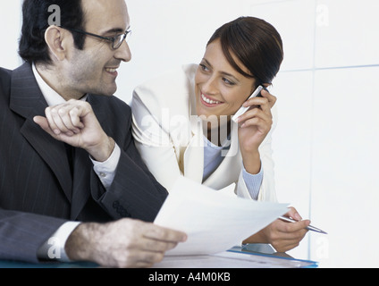 Businesswoman talking on cell phone smiling at businessman next to her Stock Photo