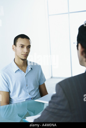 Man in short sleeves with serious expression sitting across table from man in suit Stock Photo