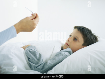 Boy in bed, woman's hand holding thermometer Stock Photo