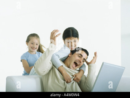 Two girls behind man sitting with laptop, one with arms around him Stock Photo