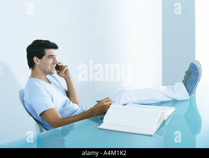 Man sitting at table with feet up, talking on phone Stock Photo