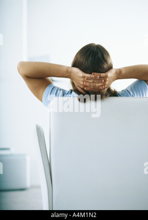 Man sitting on sofa with hands behind head, rear view Stock Photo
