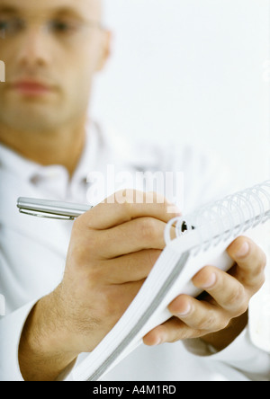 Man in white jacket taking notes, focus on hands in foreground Stock Photo