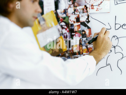 Man writing on board with images taped to it Stock Photo