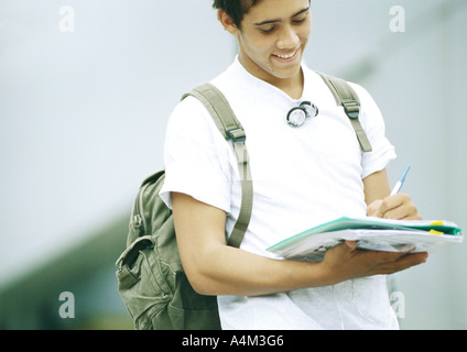 Male student standing and writing on folder Stock Photo