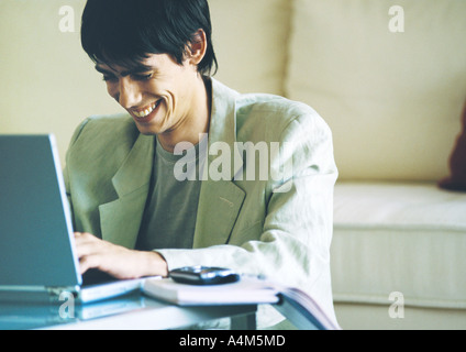 Young man smiling, using laptop on coffee table Stock Photo