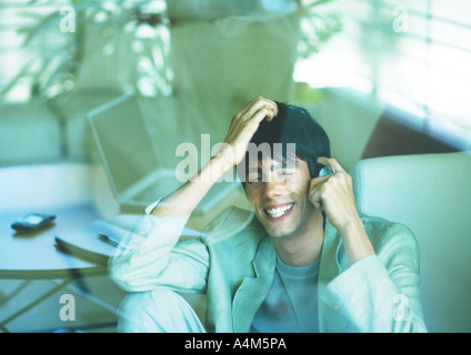 Man smiling, using cell phone, seen through glass pane Stock Photo